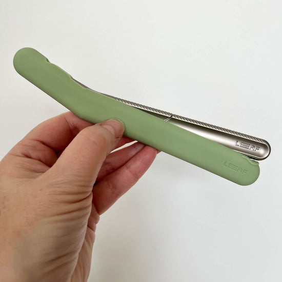 the leaf dermaplaner cover in green silicone being helo by a hand - the dermaplaner is partially in the cover