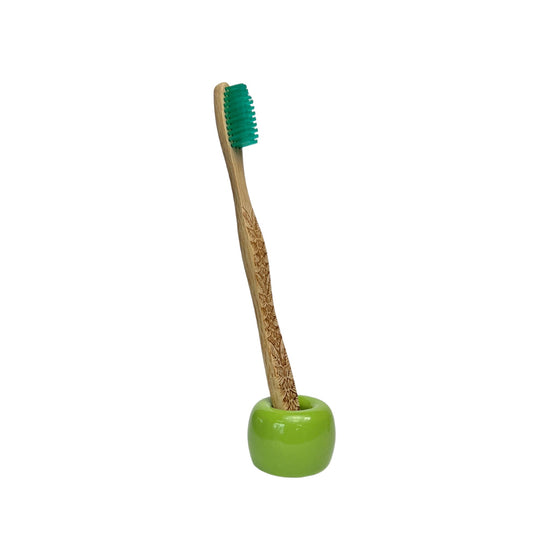 small ceramic toothbrush holder in glossy green finish holding a bamboo toothbrush